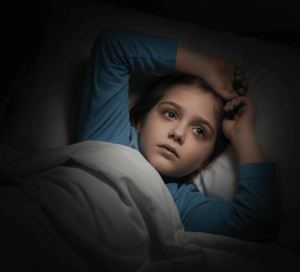 Niño acostado en la cama sin poder dormir por trastornos del sueño infantil